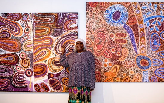 female artist stands in front of two purple, red and orange coloured painting