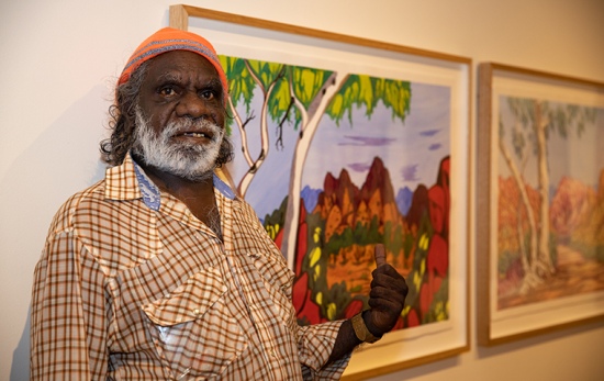 male artist stands in front of watercolour painting of central australia