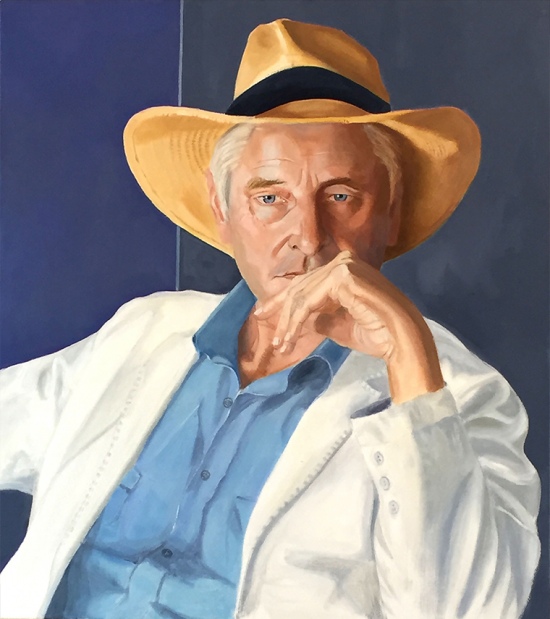 white man sitting down with wide brim hat on, hand covering his mouth
